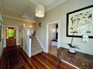 Um corredor com piso de madeira, escada, tapete estampado e um console decorativo com uma planta.