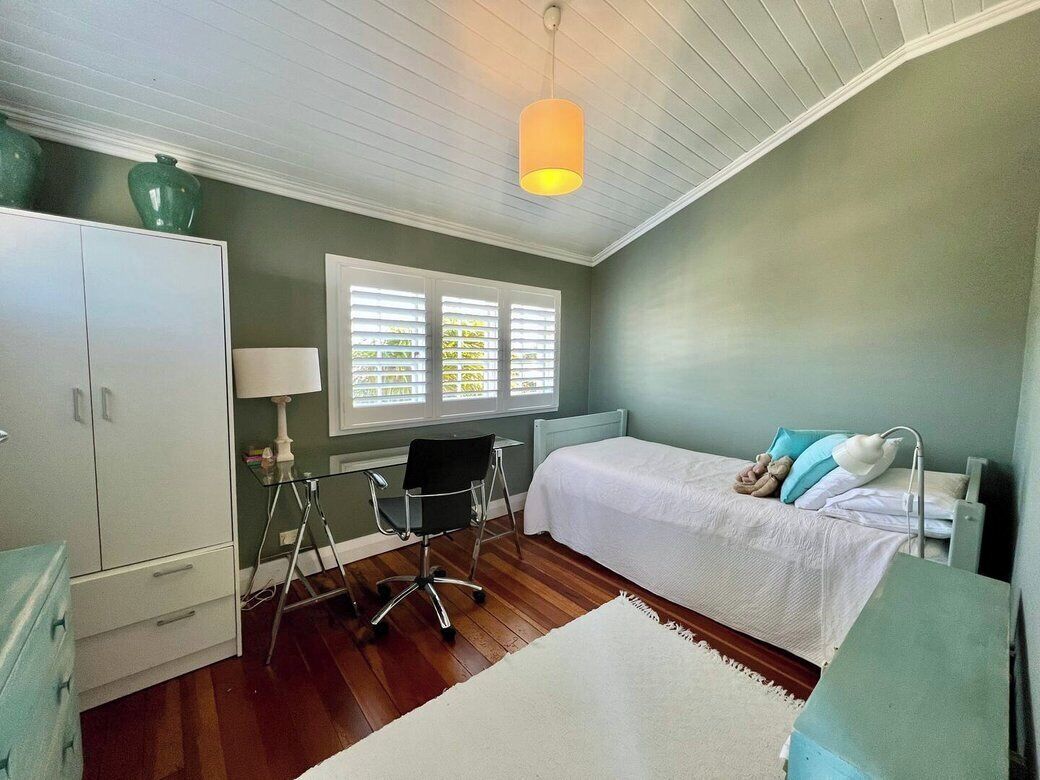 A bedroom with a bed, a desk, a chair, a lamp, and a window with blinds.