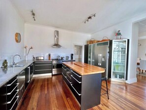 Uma cozinha moderna com armários pretos, ilha com bancada de madeira, eletrodomésticos de aço inoxidável e piso de madeira.