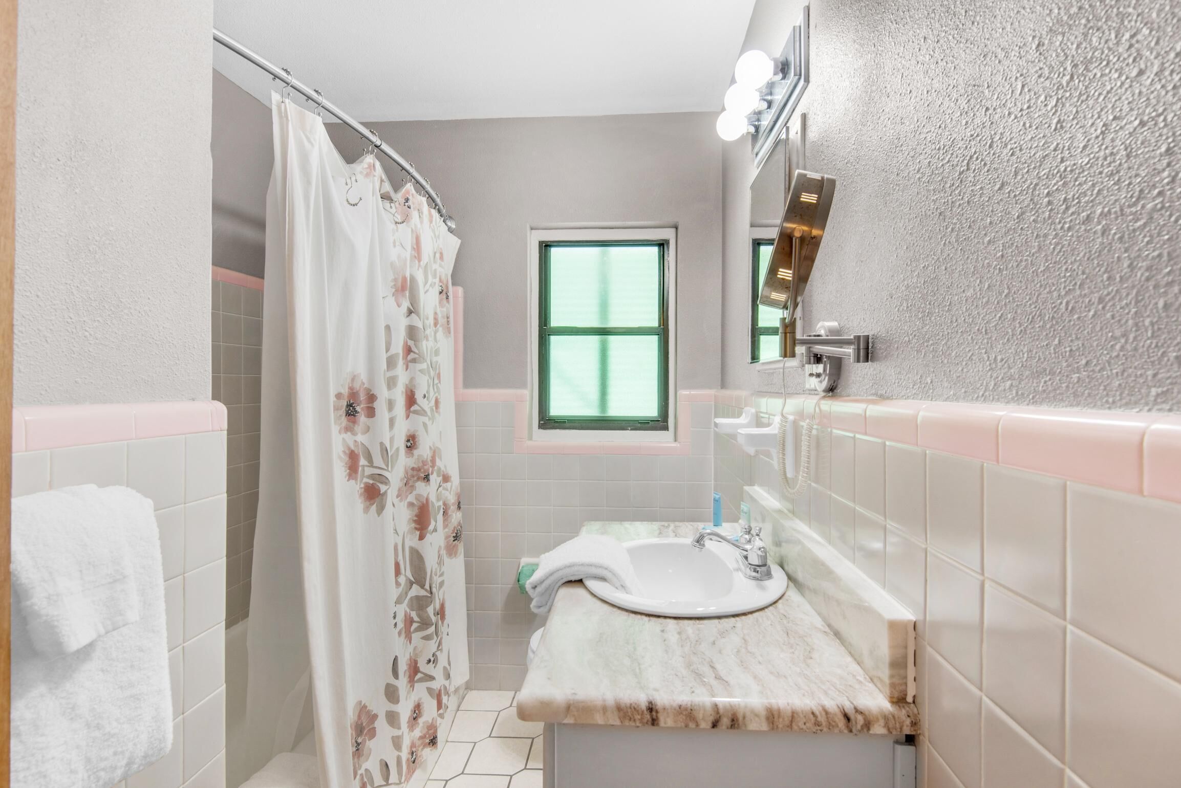 Une salle de bain avec une douche, un lavabo avec un miroir et une fenêtre.