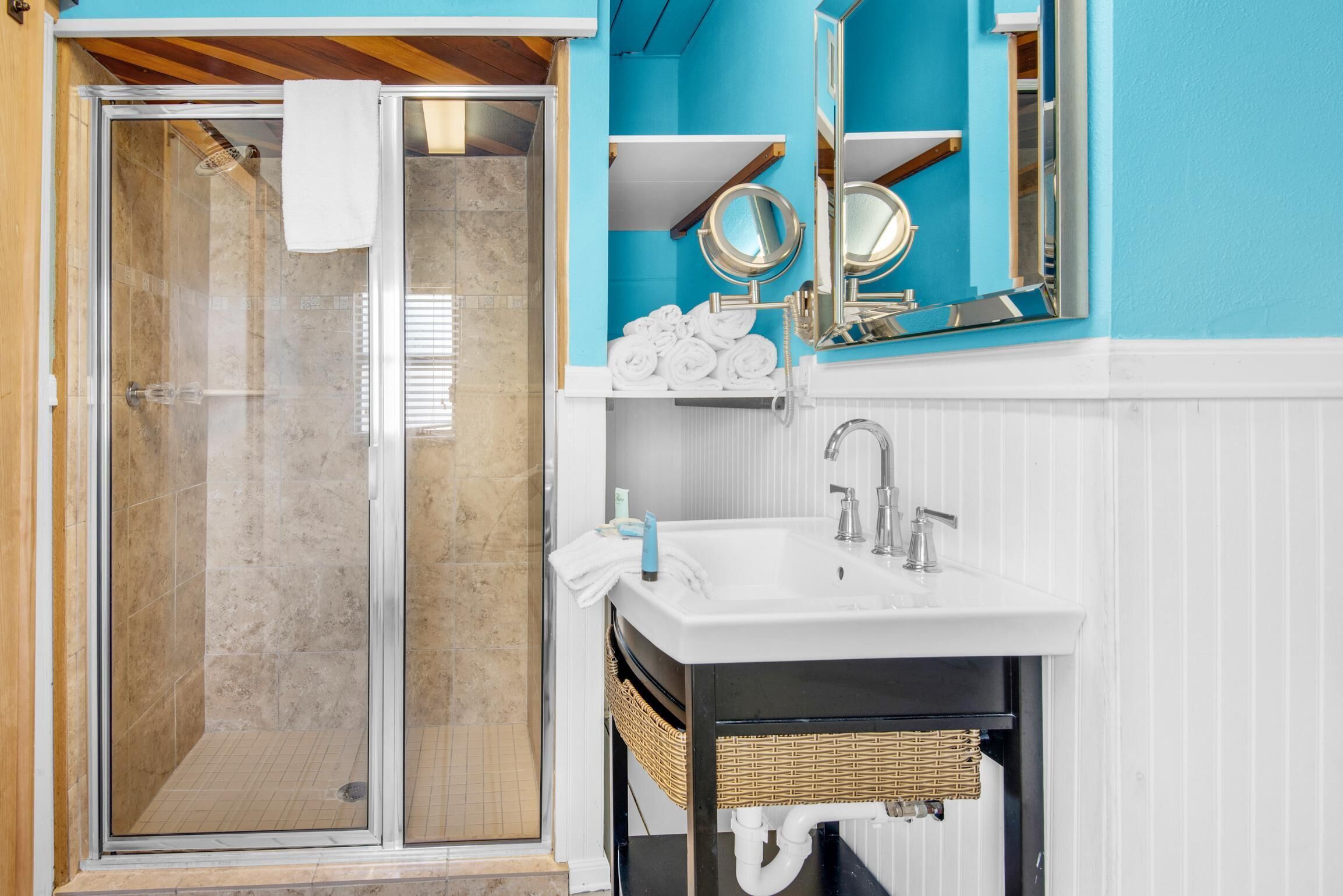 A bathroom with a glass shower enclosure, a white sink with a mirror, and a blue accent wall.