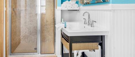 A bathroom with a glass shower enclosure, a white sink with a mirror, and a blue accent wall.