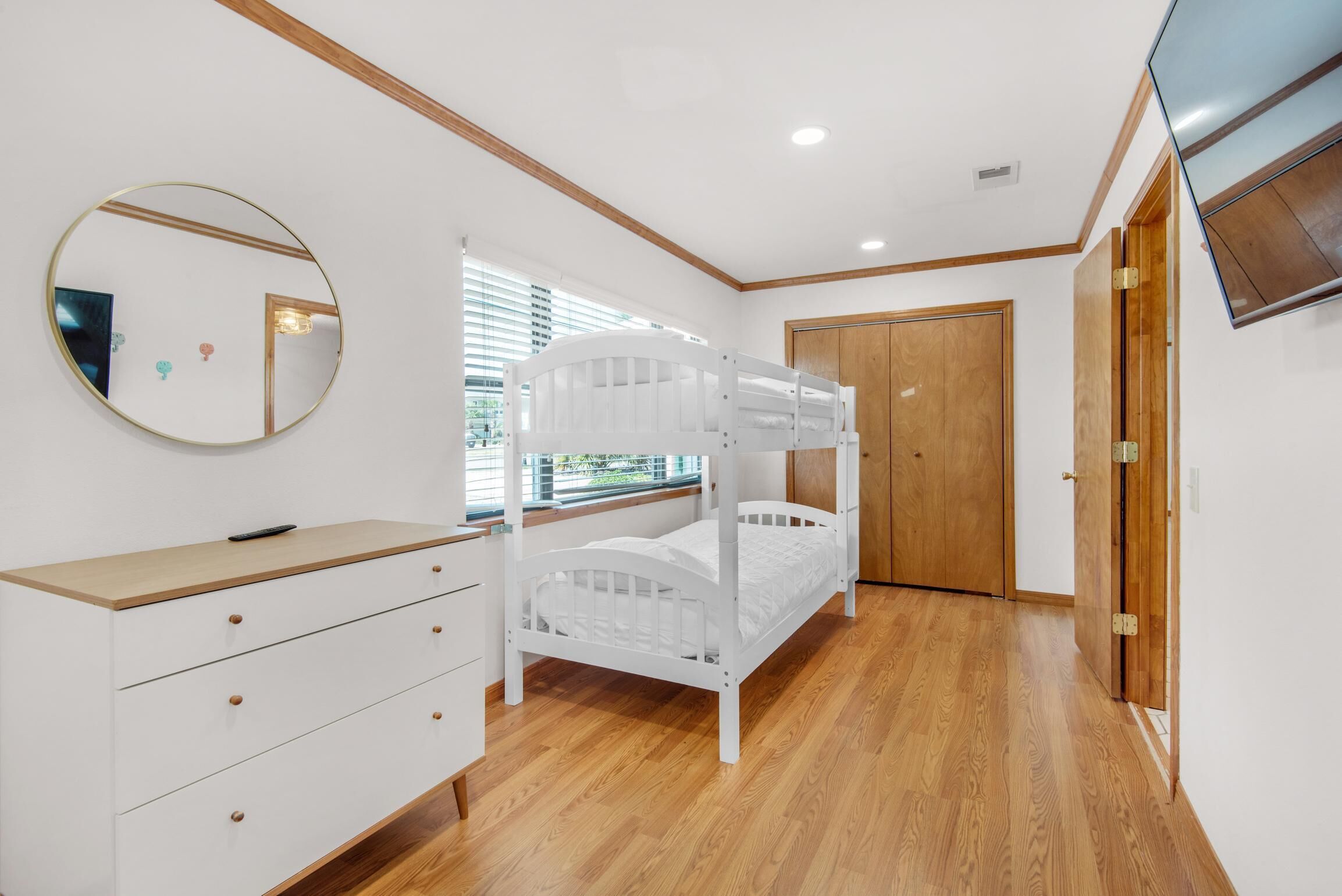 A bedroom with a bunk bed, a dresser with drawers, a round mirror, and a wooden door.