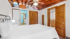 A bedroom with a large bed, wooden ceiling beams, a ceiling fan, and wooden wardrobes. - The Sugar Shack (Pensacola Beach)