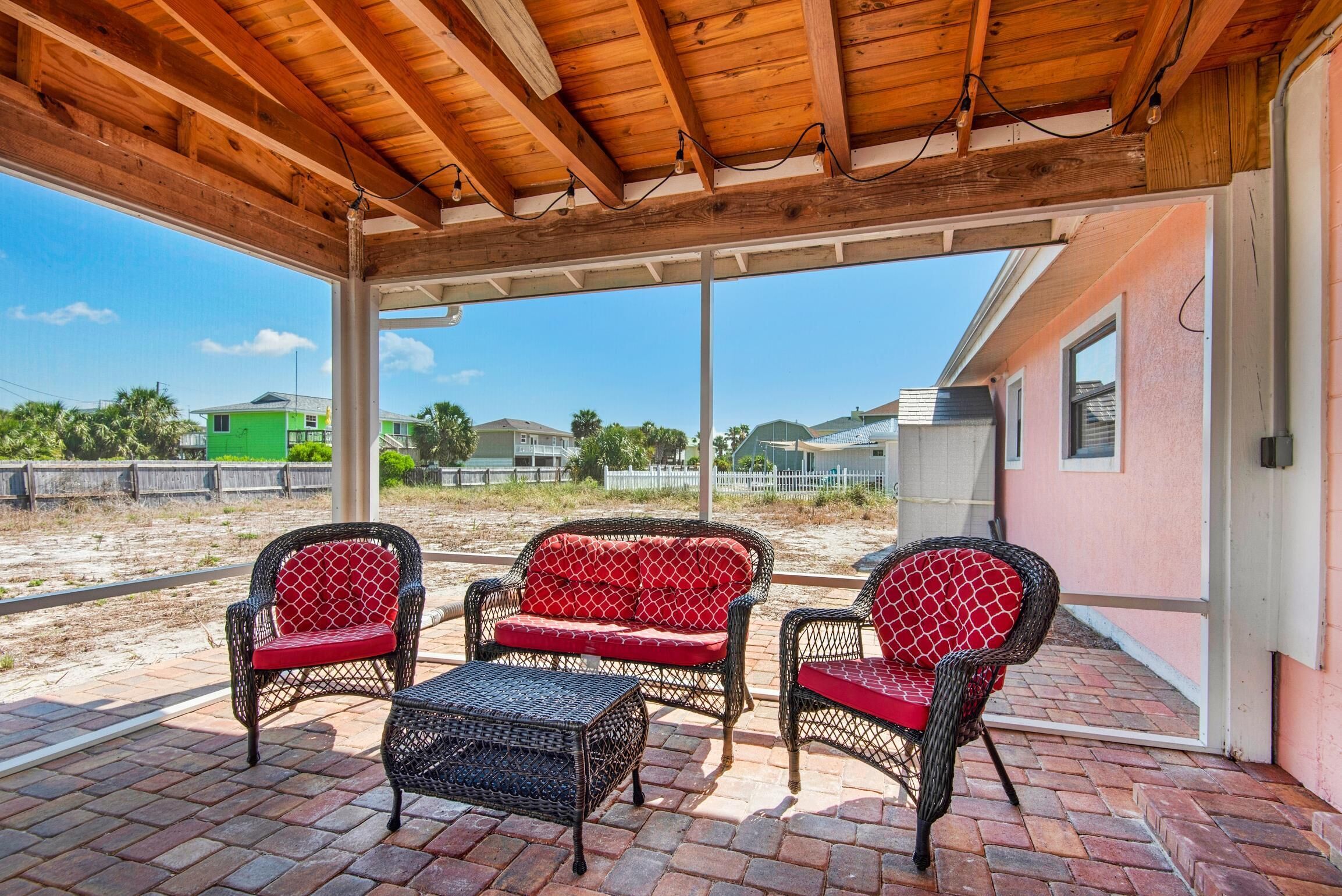 A covered patio with wicker furniture and a brick floor.