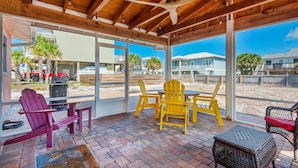 A covered patio with wooden beams, a ceiling fan, and a table with chairs. - The Sugar Shack (Pensacola Beach)