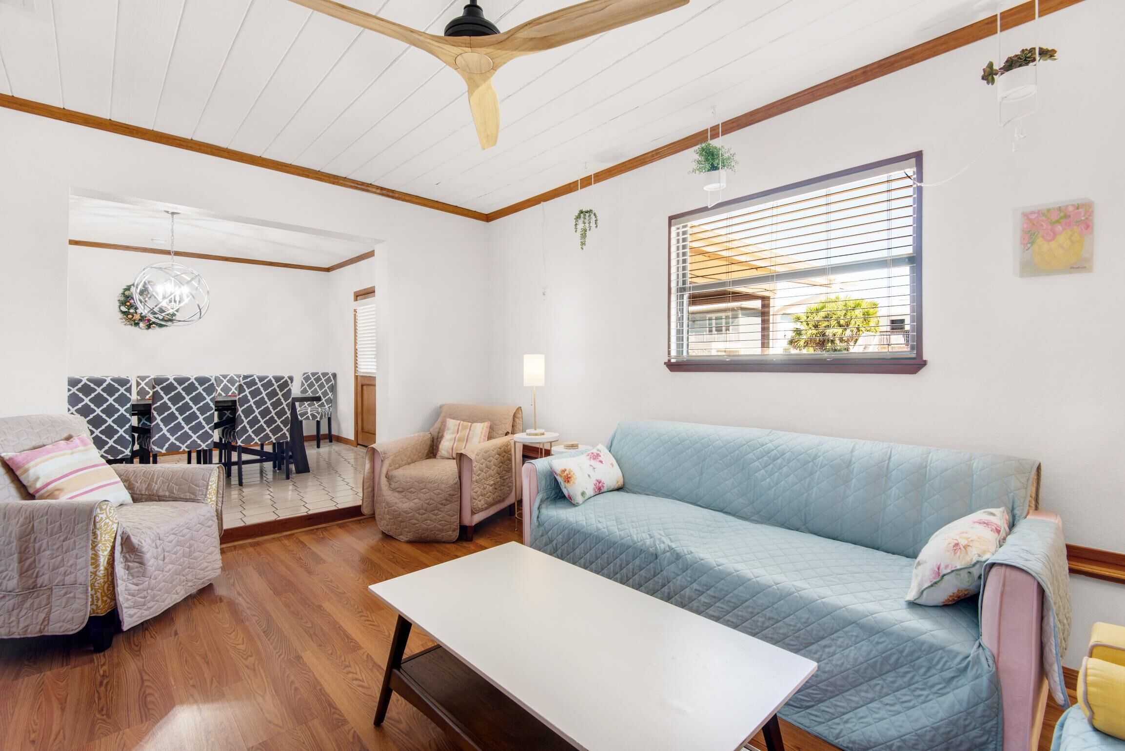 Una sala de estar acogedora con techo de madera, un sofá azul, un sillón color beige, una mesita y un comedor con papel tapiz estampado.