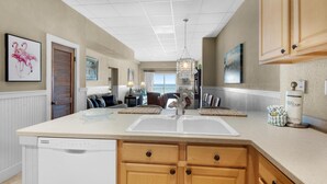 A kitchen with a central island, wooden cabinets, a dishwasher, and a chandelier. - Sans Souci Unit 405 (Pensacola Beach)