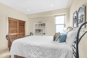 A bedroom with a large bed, a wooden wardrobe, a white bookshelf, and a window with blinds. - Sans Souci Unit 405 (Pensacola Beach)