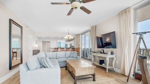 A spacious living room with a sectional sofa, a wooden coffee table, a ceiling fan, and a large TV on the wall.