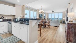 A spacious kitchen with white cabinets, a granite countertop, and a dining area with wooden chairs and a gray sofa.