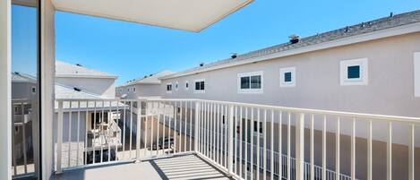A balcony with a white railing, a covered area, and a view of neighboring buildings.