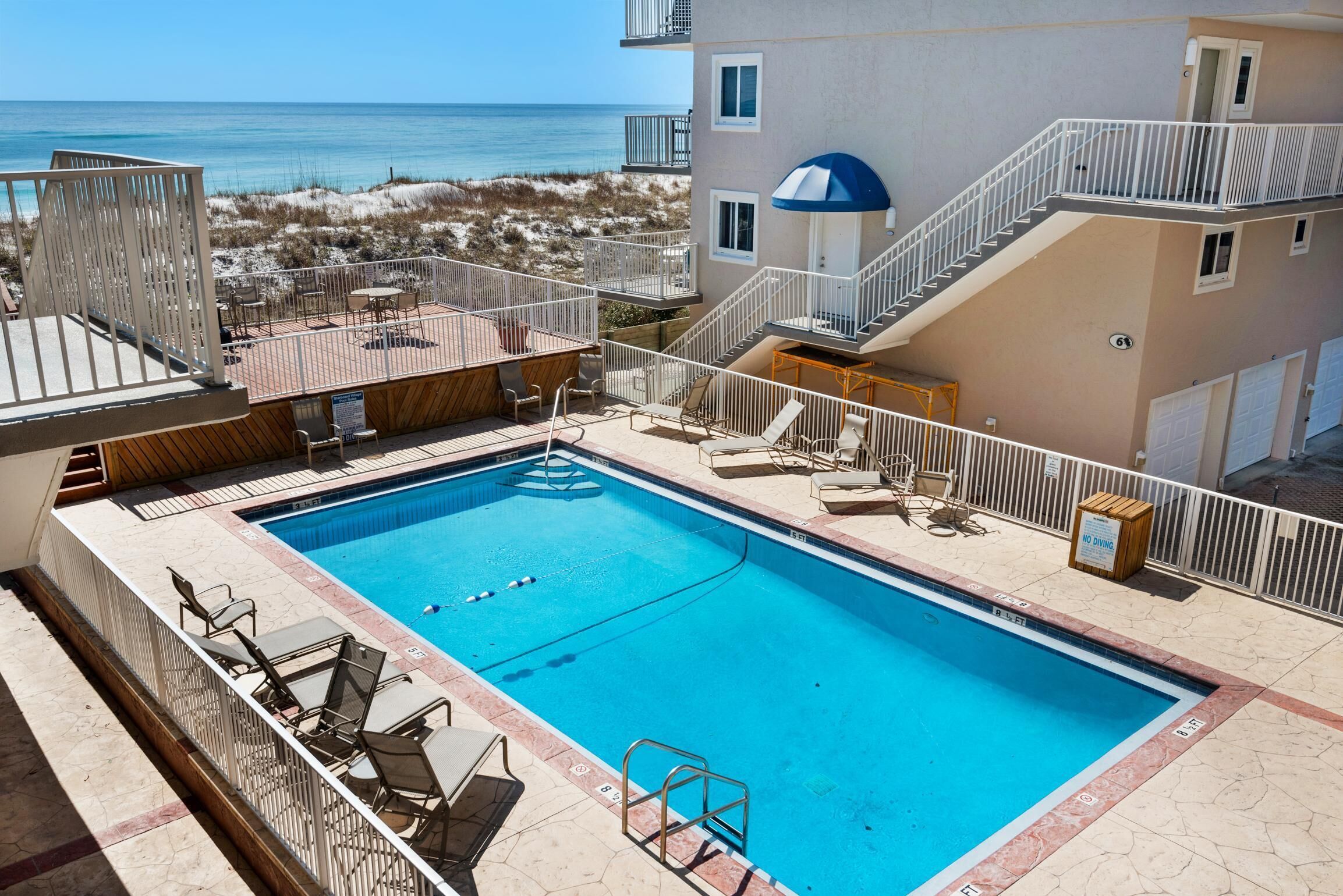 A swimming pool with a view of the beach and ocean, surrounded by outdoor seating and a staircase.