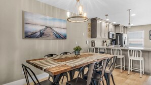 A dining area with a wooden table, black chairs, a chandelier, and a large painting on the wall. - Deep Water Cove 103 - OLD (Pensacola Beach)