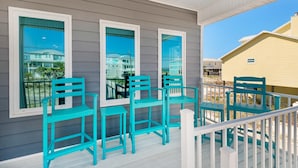 A covered porch with teal chairs and a white railing.