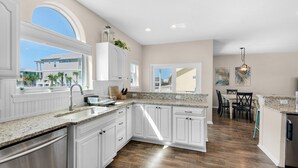 A spacious kitchen with white cabinetry, granite countertops, and a view of the outside.