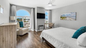 A bedroom with a bed, a desk, a chair, a TV, and a window with a view.