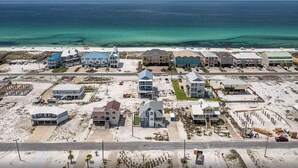 An aerial view of a coastal residential area with houses, a beach, and a clear view of the ocean.