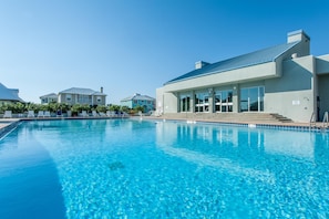 A swimming pool with clear blue water, surrounded by lounge chairs and a building with large windows.