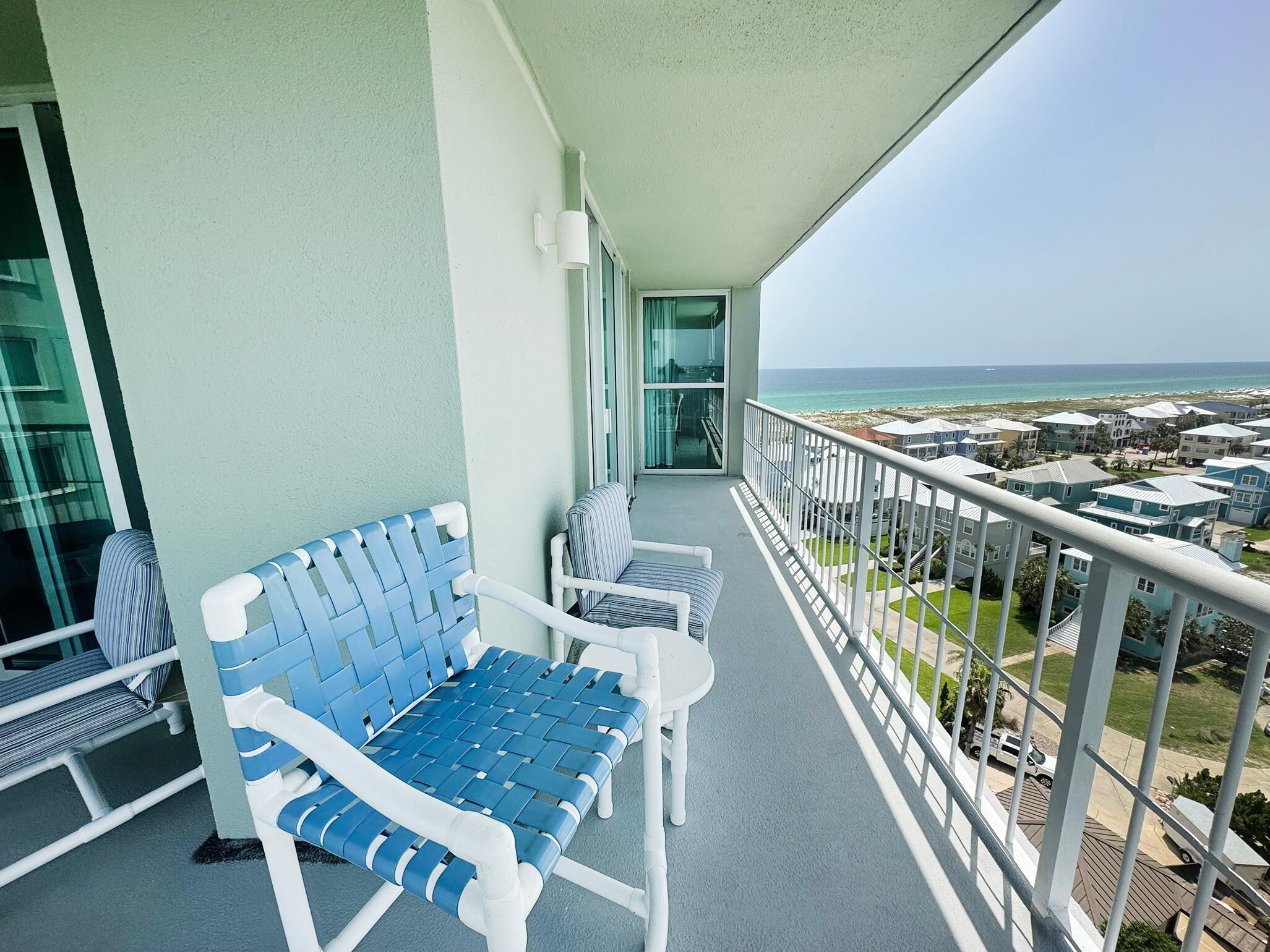 A balcony with a blue and white chair, a white table, and a view of the ocean and buildings.