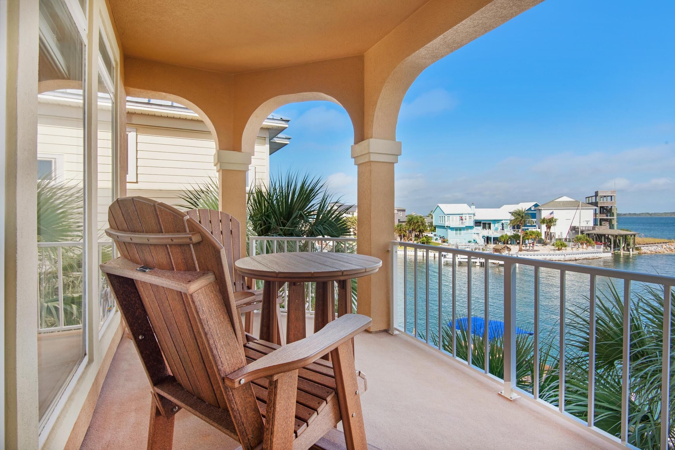 A wooden chair and table on a balcony with a view of a beach and ocean.