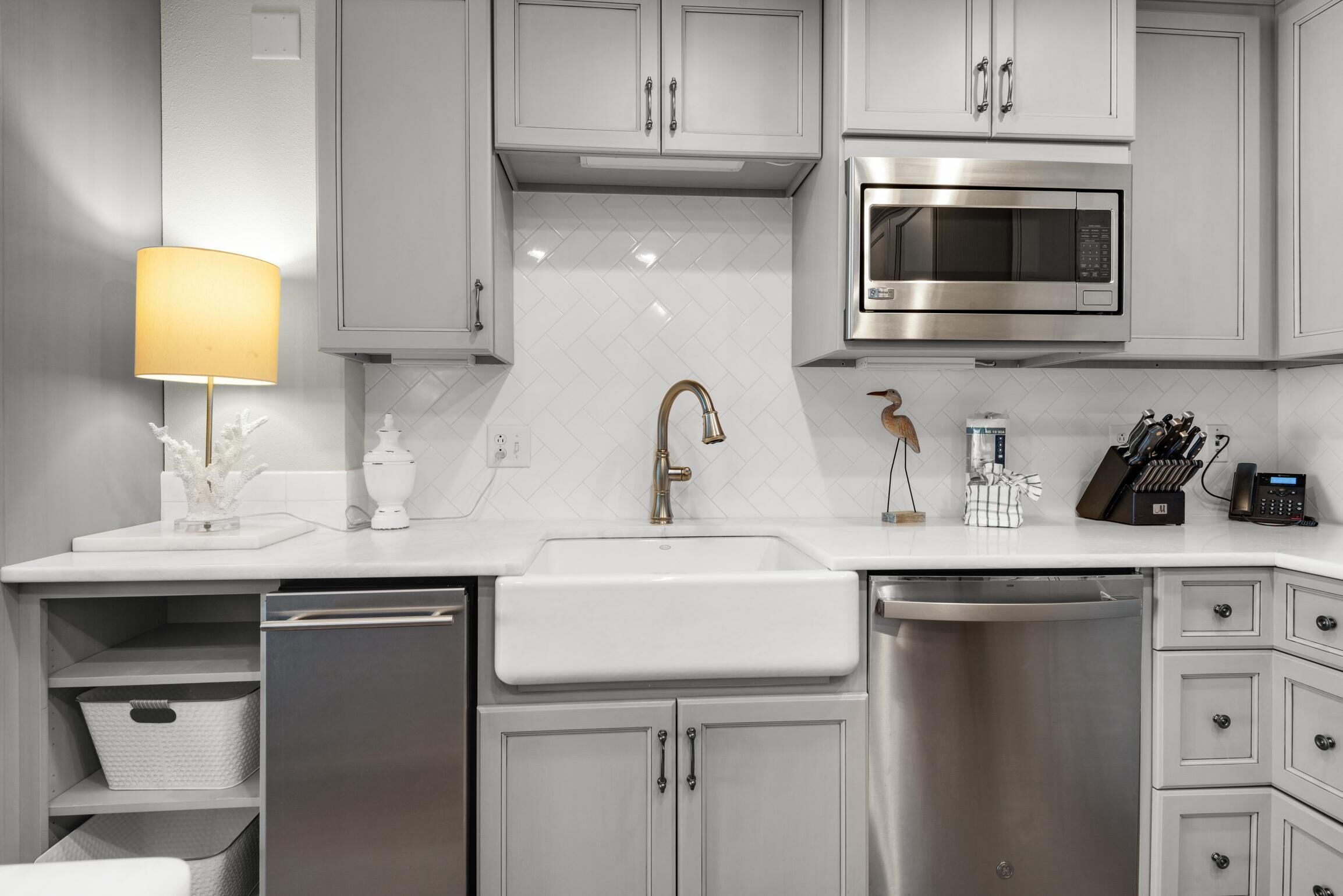 A modern kitchen with white cabinetry, a stainless steel dishwasher, a sink, a microwave, and a coffee machine.