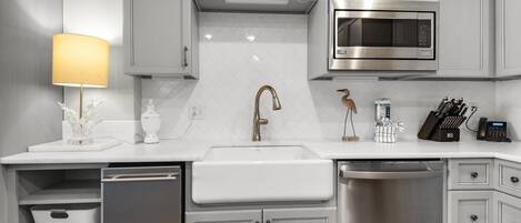 A modern kitchen with white cabinetry, a stainless steel dishwasher, a sink, a microwave, and a coffee machine.