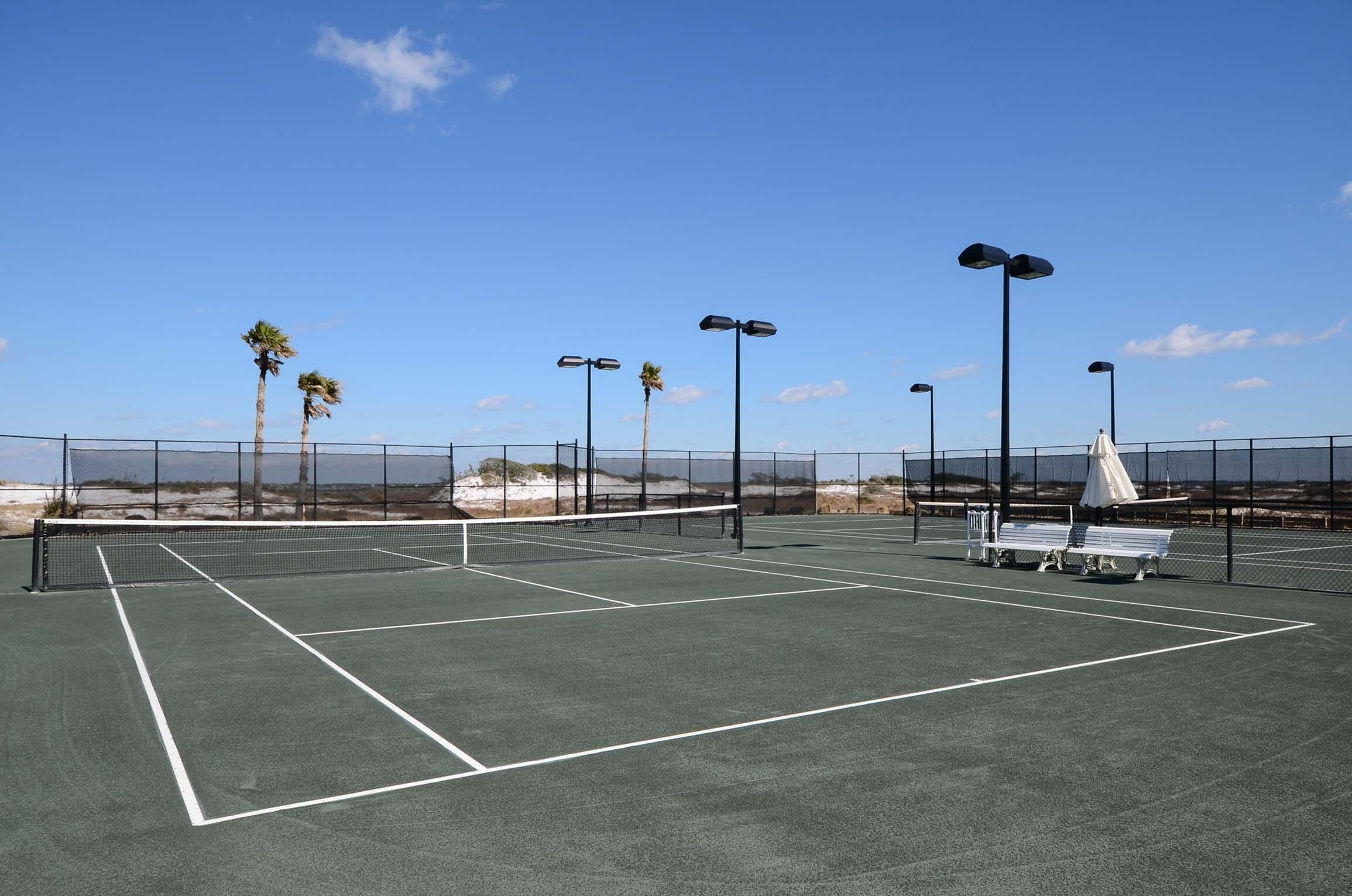A tennis court with a net, benches, and street lamps.
