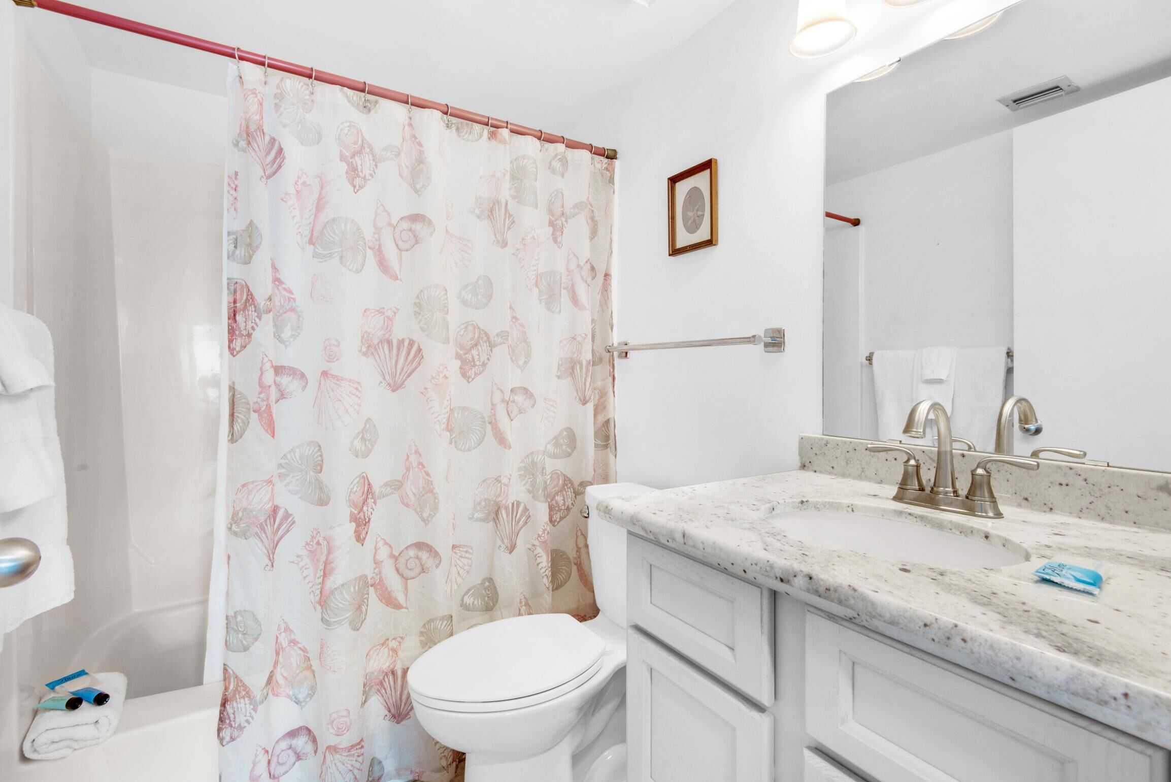 A bathroom with a toilet, sink, and shower curtain with a shell pattern.