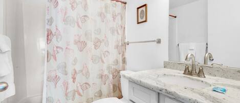 A bathroom with a toilet, sink, and shower curtain with a shell pattern.