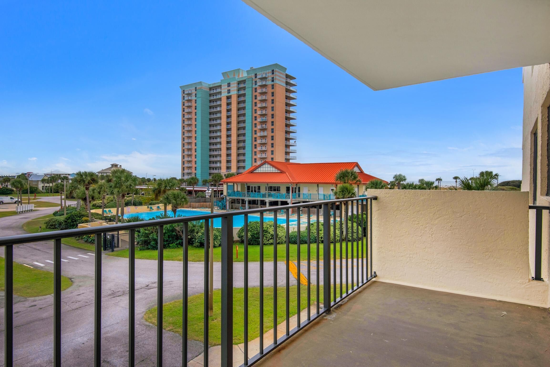A balcony with a view of a swimming pool, a tall residential building, and a red-roofed building.