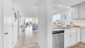 A modern kitchen with white cabinets, a dishwasher, and a large window. - Santa Rosa Dunes 1021 (Pensacola Beach)