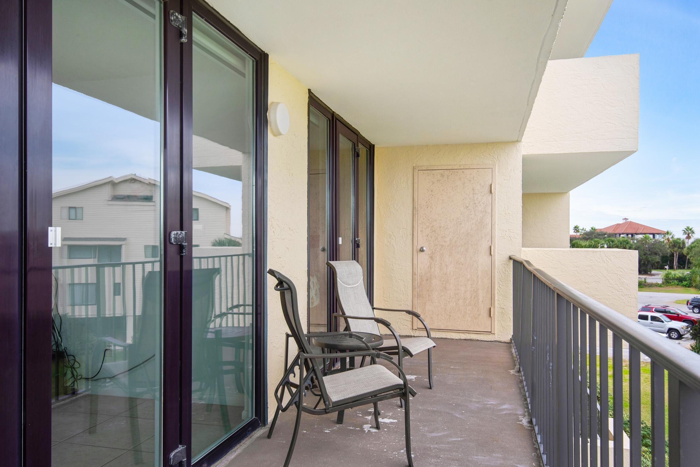 A balcony with two chairs and a table, a sliding glass door, and a beige wall.