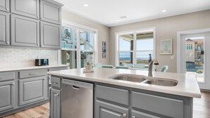Una cocina moderna con armarios grises, lavavajillas y un amplio ventanal con vistas al mar.