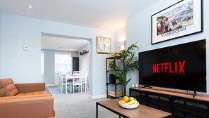 A living room with a sofa, a coffee table with fruit, a TV displaying 'NETFLIX', a clock, and a framed picture on the wall. - Waimea Apartment 4 | Best Sea View, Beach Front, Parking, Scarborough (North Yorkshire)