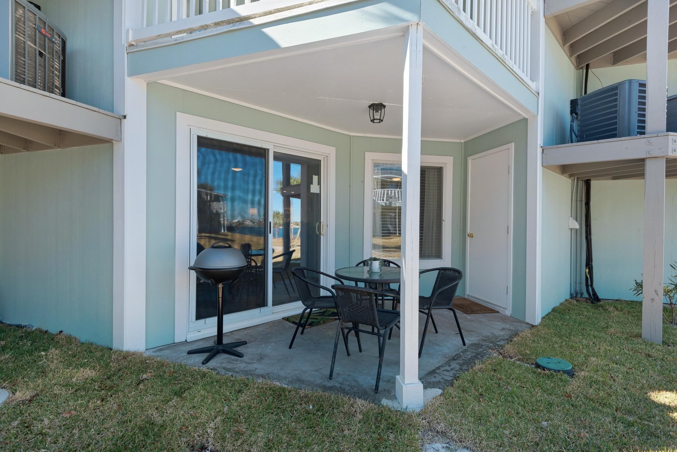 En overdækket terrasse med et bord, stole, grill og en skydedør til en balkon.