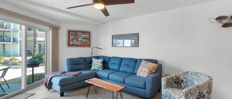 A living room with a blue sectional sofa, a wooden coffee table, a patterned armchair, and a ceiling fan.