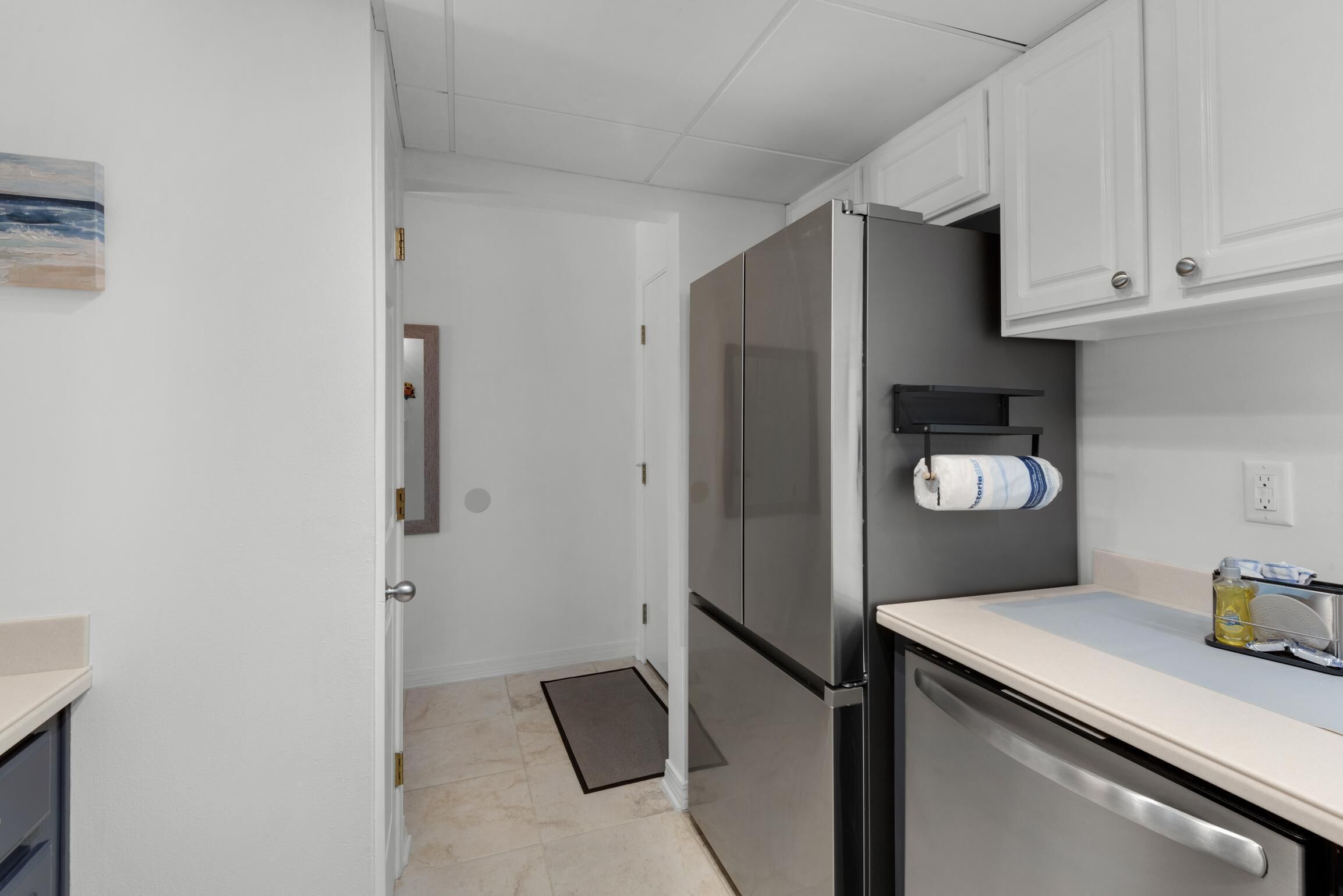 A compact kitchen with white cabinets, a stainless steel refrigerator, and a dishwasher.