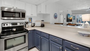 Een moderne keuken met witte kastjes, een roestvrijstalen magnetron, een fornuis en een aanrecht met een koffiezetapparaat en blender.