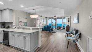 A spacious kitchen with a large island, a dining area with blue chairs, and a view of the ocean.
