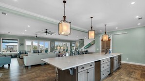 A spacious kitchen with a large island, modern pendant lights, and a view to the living area. - Emerald Oasis (Pensacola Beach)