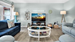 A living room with a TV, a glass coffee table, a blue sofa, and a grey sofa. - Beachview 101- Beaches and Moonbeams (Navarre)