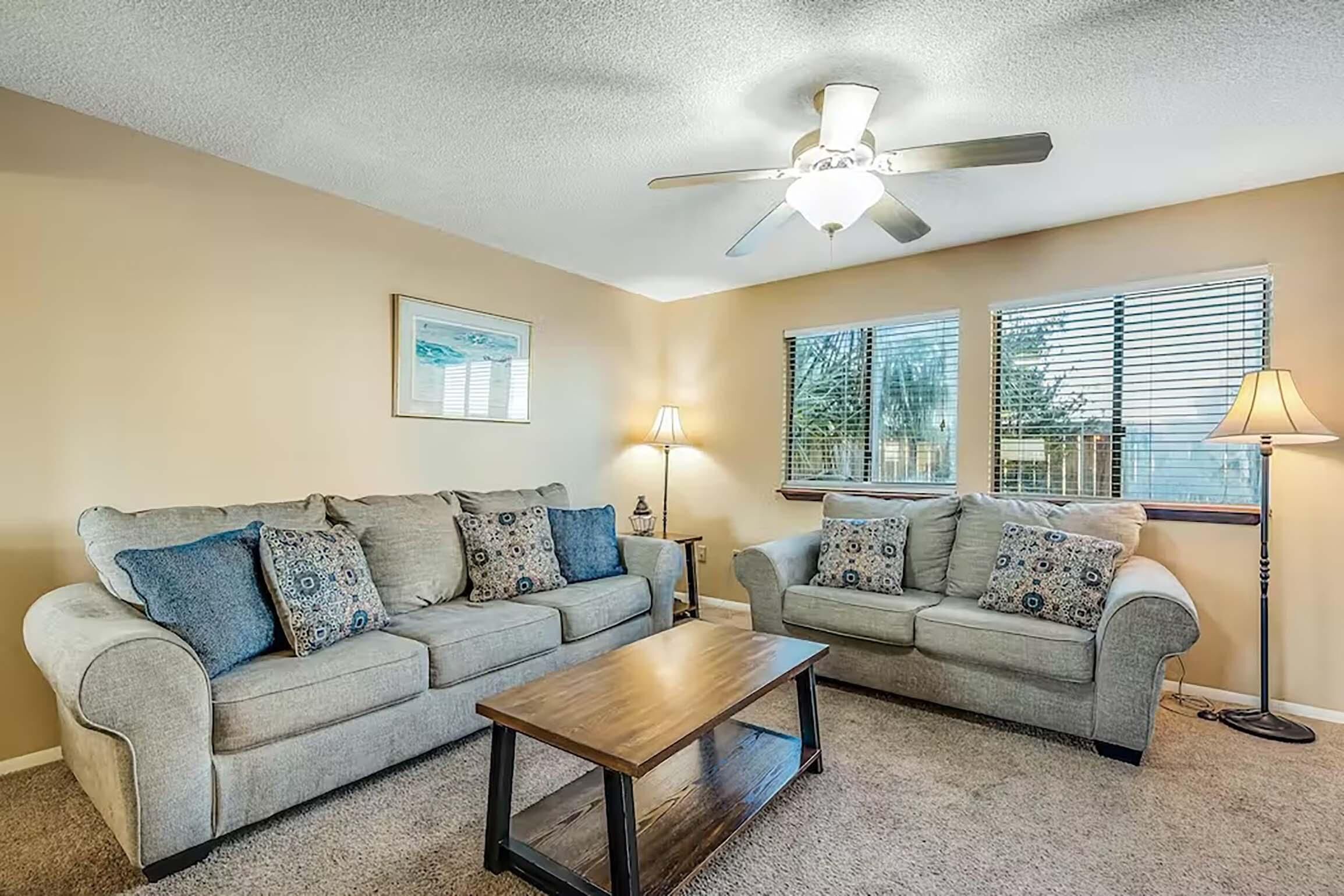 A living room with two grey sofas, a wooden coffee table, a ceiling fan, and two floor lamps.