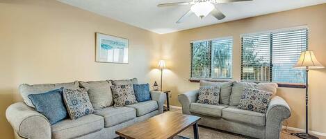 A living room with two grey sofas, a wooden coffee table, a ceiling fan, and two floor lamps.