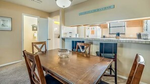 Un comedor con mesa y sillas de madera, una lámpara colgante y una zona de cocina con armarios y encimera.