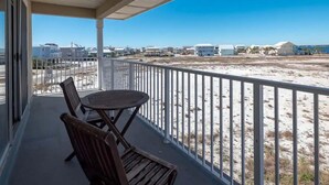 A balcony with a table and chairs, overlooking a sandy beach and a row of houses. - Sunset Harbor Villas 431 (Navarre)