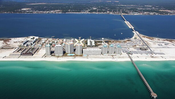 An aerial view of a coastal area with a marina, several high-rise buildings, and a long pier extending into the water. - Sunset Harbor Villas 431 (Navarre)