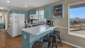 A kitchen with teal cabinets, a white refrigerator, a microwave, and a window with a view of a beach. - Sunset Harbor Villas 431 (Navarre)