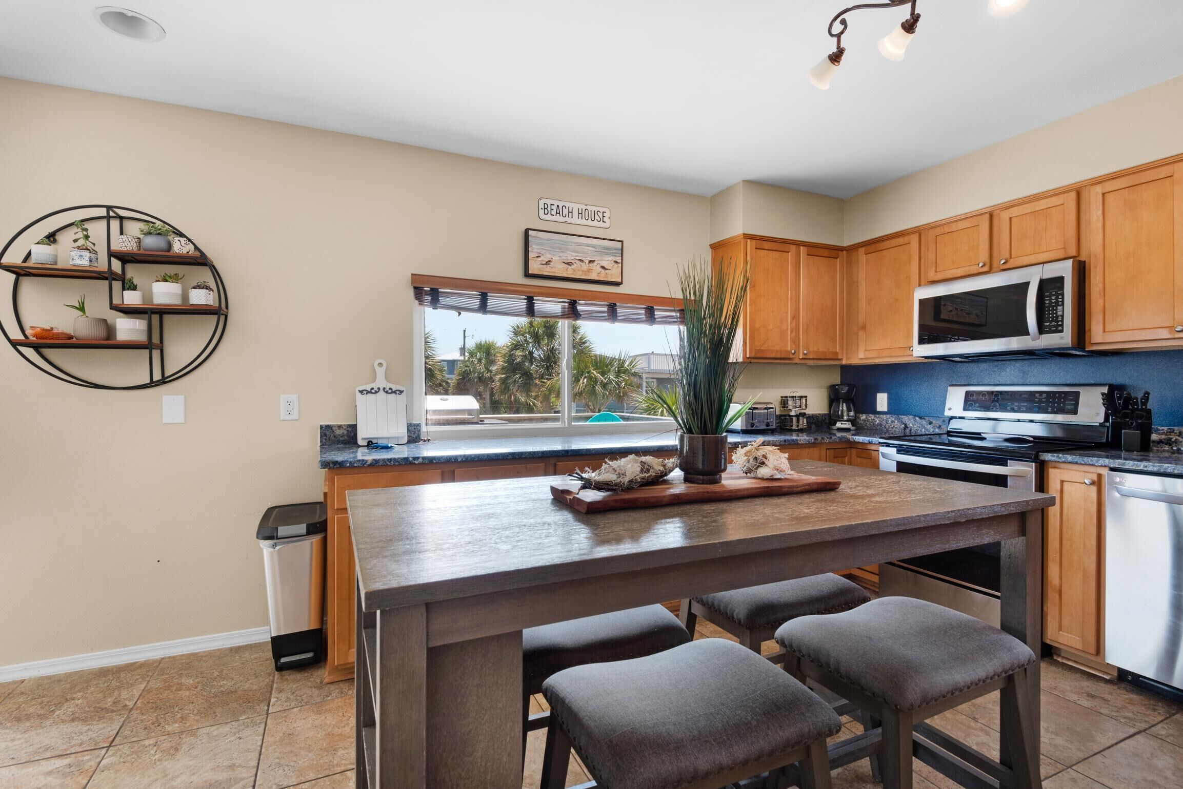 A modern kitchen with wooden cabinets, a central island with bar stools, a built-in microwave, and a view of the outdoors through large windows.