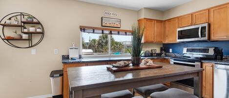 A modern kitchen with wooden cabinets, a central island with bar stools, a built-in microwave, and a view of the outdoors through large windows.